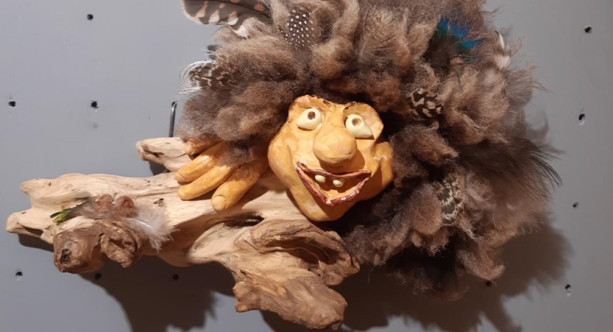 Waldschratt, hergestellt aus einem Holzstück, dem ein Gesicht und Hände aus Keramik gegeben wurde. Fell und Federn schmücken den Kopf.